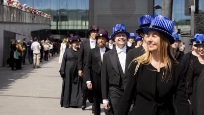 Musiikintohtoreita promootiokulkueessa sinisissä musiikintohtorin hatuissaan Musiikkitalon ulkopuolella.