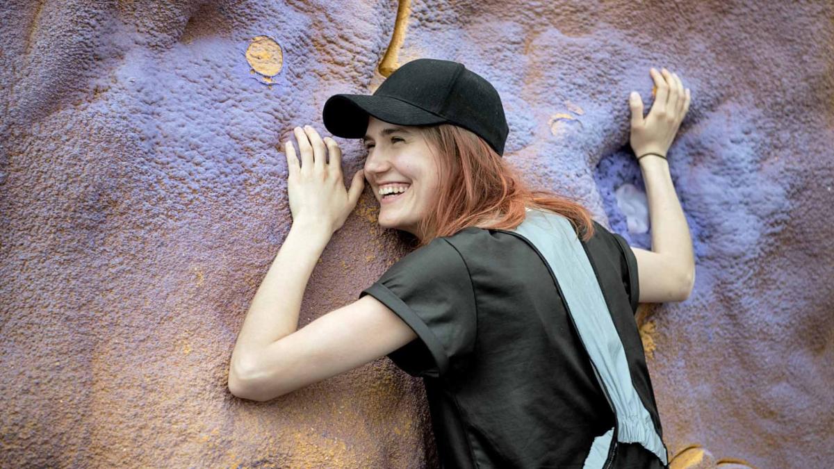 Nainen seisoo seinää vasten ja nauraa.