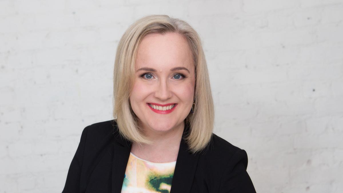 Eveliina Sumelius hymyilee valkoista seinää vasten.