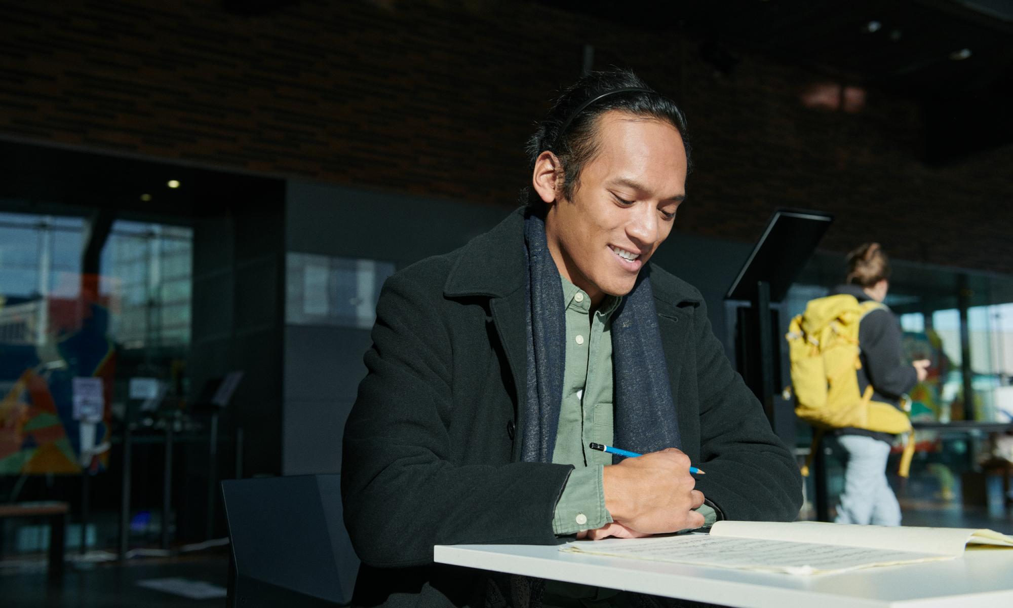 mies kirjoittaa pöydän ääressä