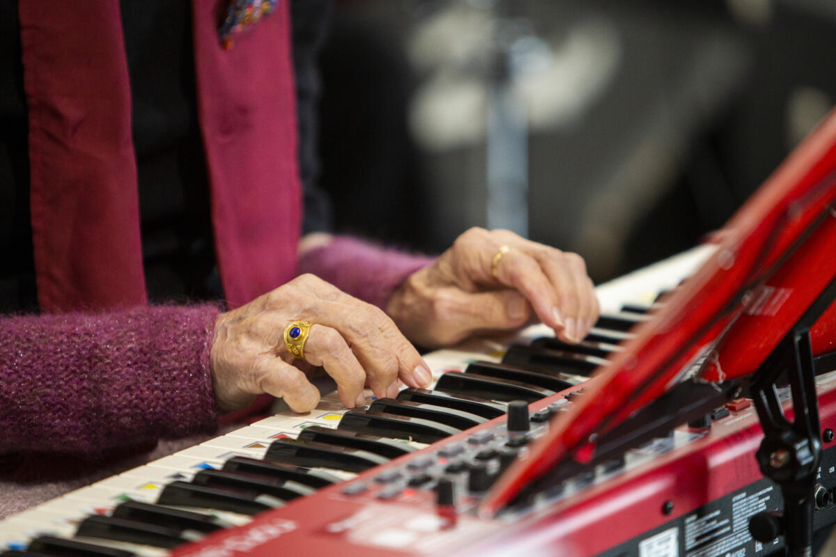 Kuva vanhan naisoletetun käsistä soittamassa sähköpianoa. Käsissä on kultaisia sormuksia ja neuletakin hiha kimaltelee.